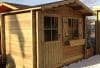 Abri de jardin en bois clair avec porte, fenêtre et jardinière.
