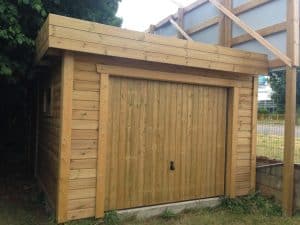 Garage en bois clair, porte fermée, toit plat.