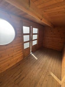 Intérieur de cabane en bois, fenêtre ronde et portes.