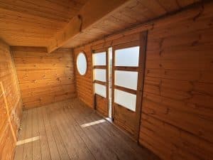 Intérieur de cabane en bois, fenêtre ronde, porte vitrée.