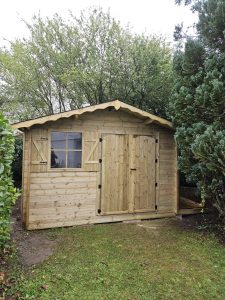 Abri de jardin en bois neuf avec volets et arbres.