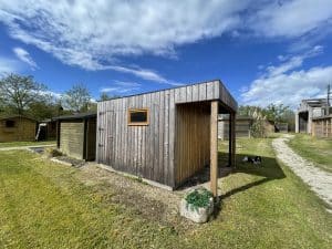 Cabanes en bois rustiques, jardin verdoyant, chien, ciel bleu nuageux.
