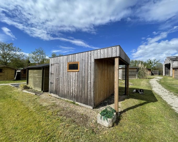 Cabanes en bois rustiques, jardin verdoyant, chien, ciel bleu nuageux.